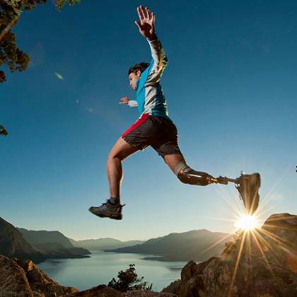 Skaczący mężczyzna na tle panoramy zawierającej góry oraz jezioro