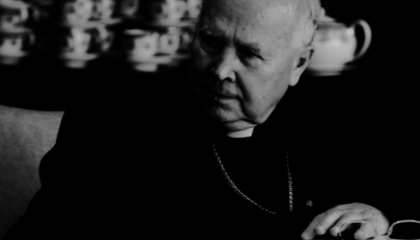 Postać arcybiskupa Tadeusza Gocłowskiego, siedzącego przy stole podczas rady nadzorczej fundacji.